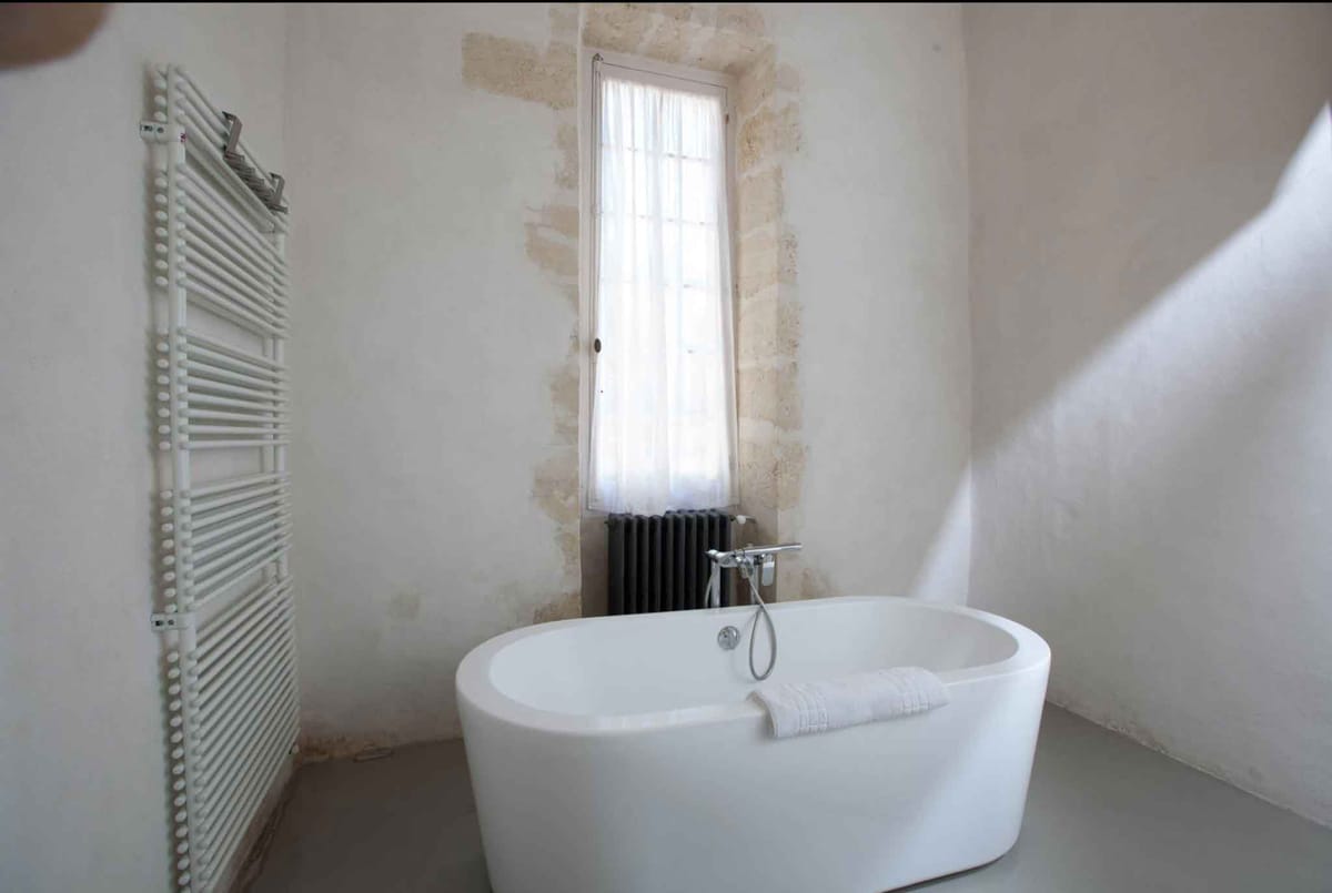 Freestanding oval tub with chrome fixtures in stone-walled chateau bathroom with sheer curtain