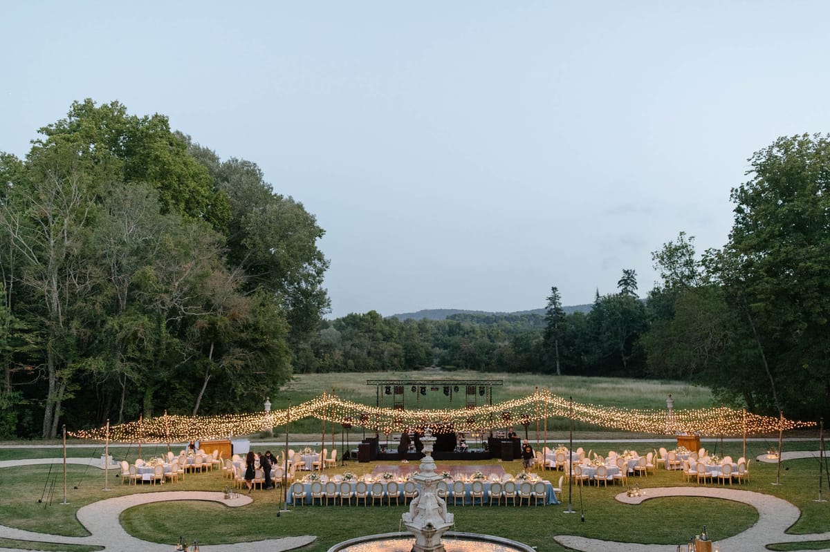 Dusk chateau garden reception with fairy light canopy gold chairs pale blue head table and stone fountain