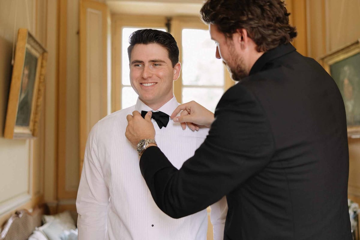 Groom getting ready with best man fixing his bow tie at Château de Bouthonvilliers