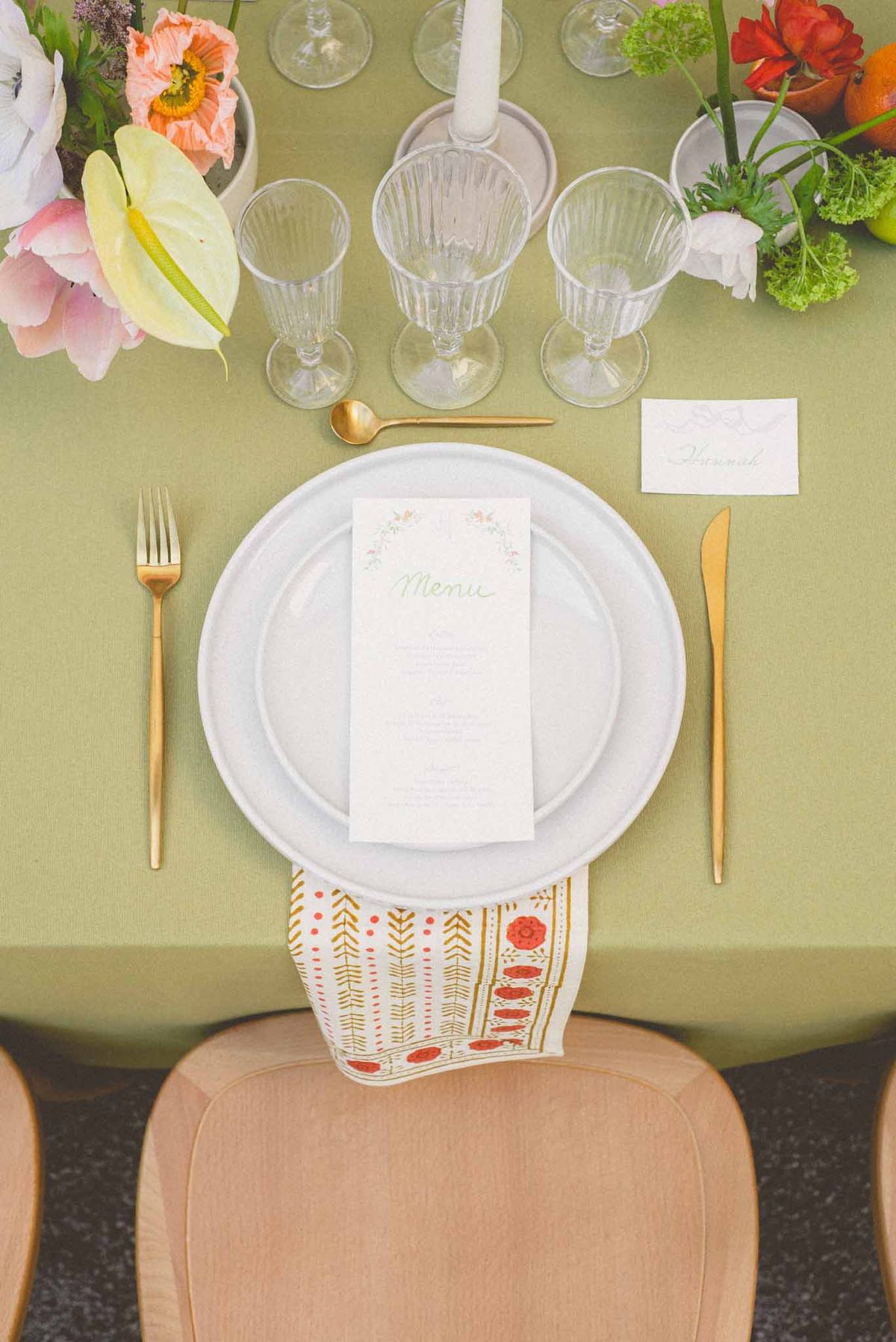 Overhead flat lay of reception place setting with gold cutlery, printed menu, and coral and pink floral arrangements