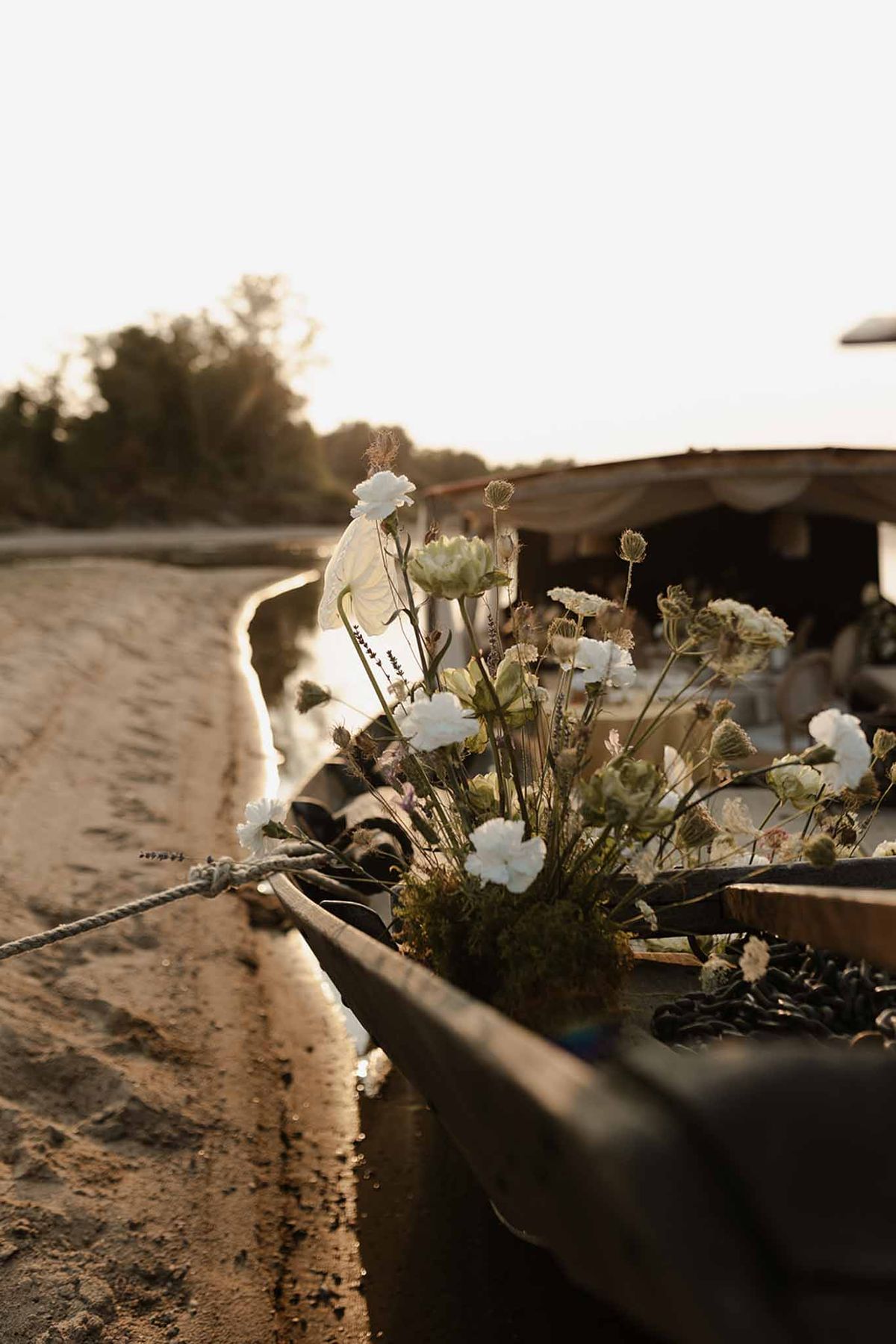 Rustic floral arrangement of ivory carnations tied to weathered wooden rail at golden hour