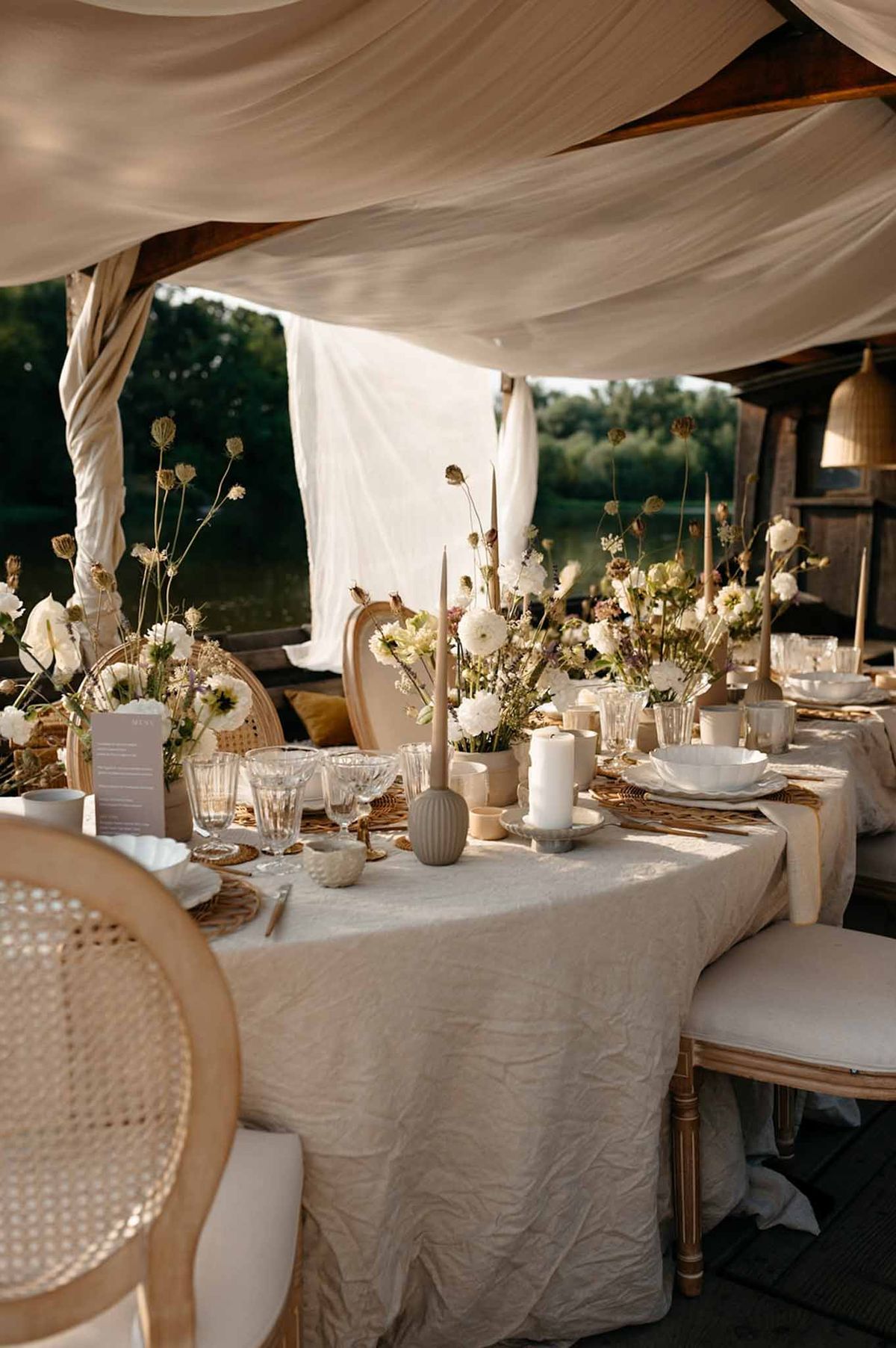 Reception table under open-sided marquee with cream draping and rattan chargers