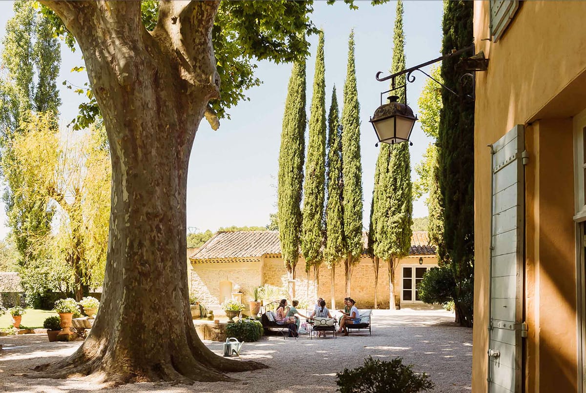Provencal bastide courtyard with ochre stone, blue-grey shutters, cypress trees, and terracotta pots