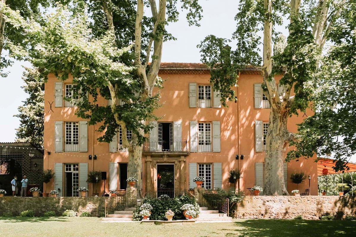 Three-storey terracotta-orange bastide with blue shutters, fairy lights, and white potted flowers at entrance