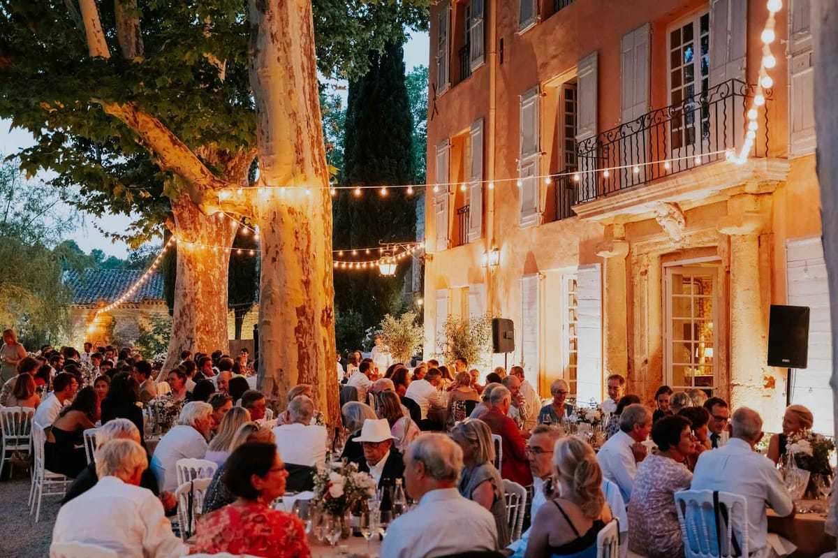 Outdoor reception dinner for 80 guests at Provencal bastide courtyard with Edison bulb string lights at dusk