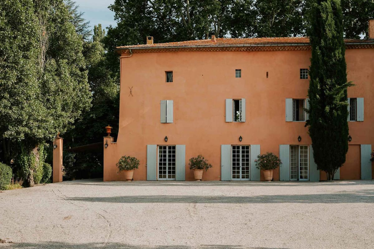 Provencal bastide with terracotta walls, sage-blue shutters, cypress trees, and gravel courtyard