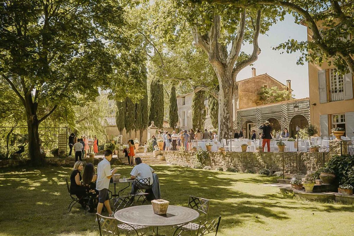 30 guests at bistro tables on Provencal bastide lawn with lattice pergola and cypress trees