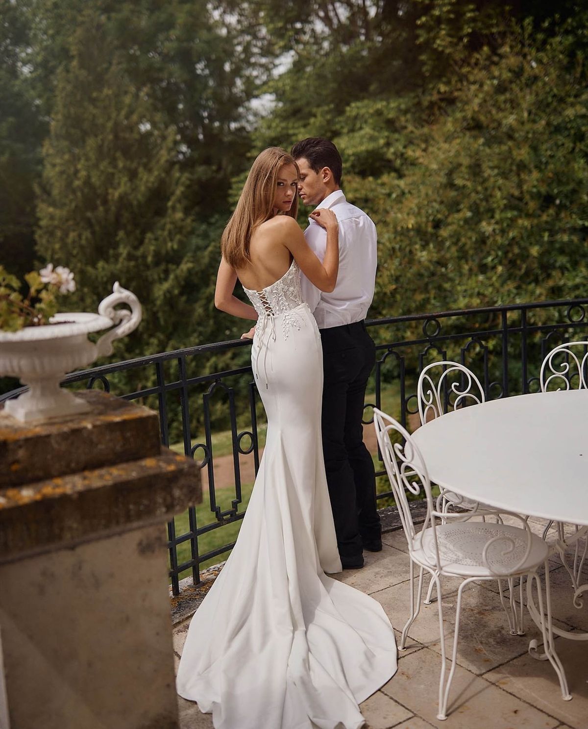 Bride in lace-back mermaid gown and groom on stone terrace with wrought iron balustrade at French manor
