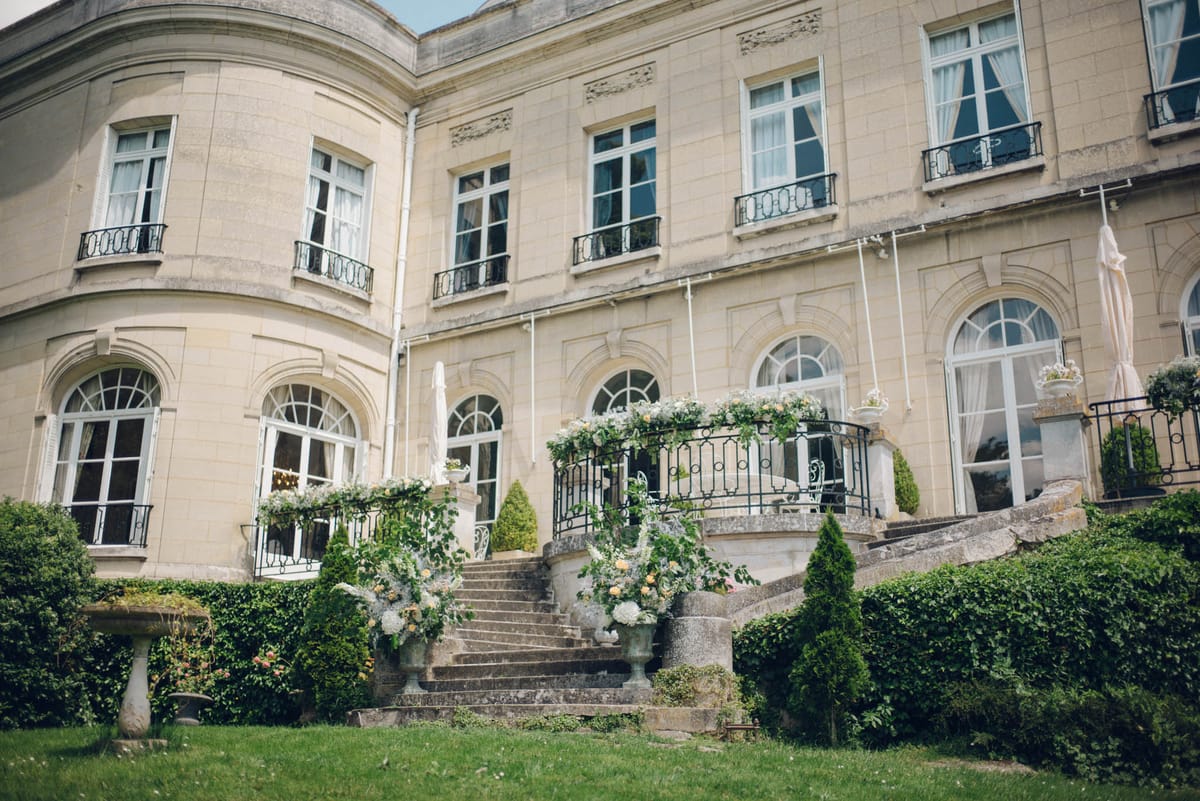 French chateau facade with curved double staircase decorated with white hydrangeas, peach roses, and a floral arch
