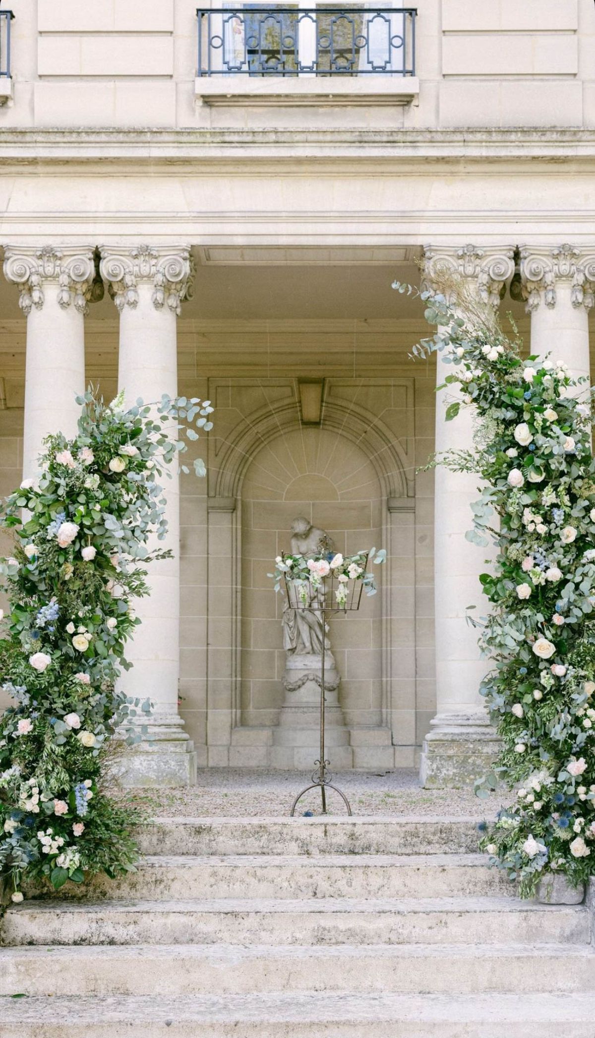 Floral columns with blush roses and blue hydrangeas framing neoclassical chateau staircase entrance