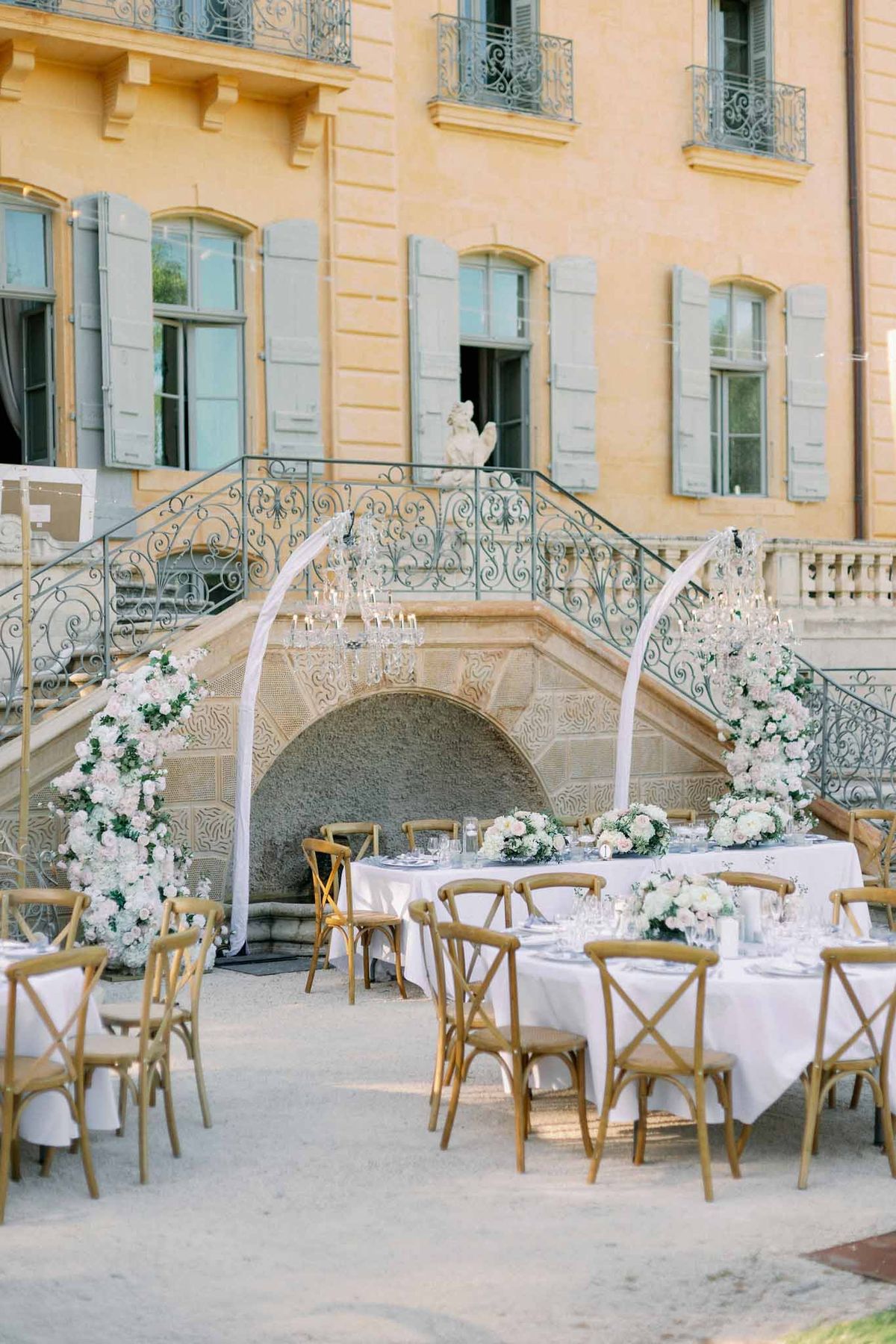 Round wooden reception table set outdoors in front of vintage château with place settings