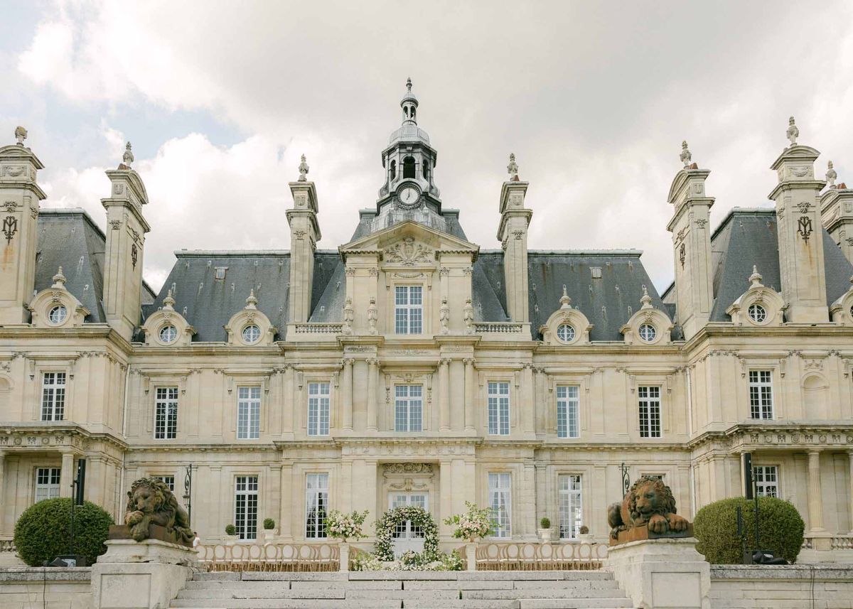 Classical chateau with Mansard roofs, blue shutters, domed clocktower, and stone lion sculptures