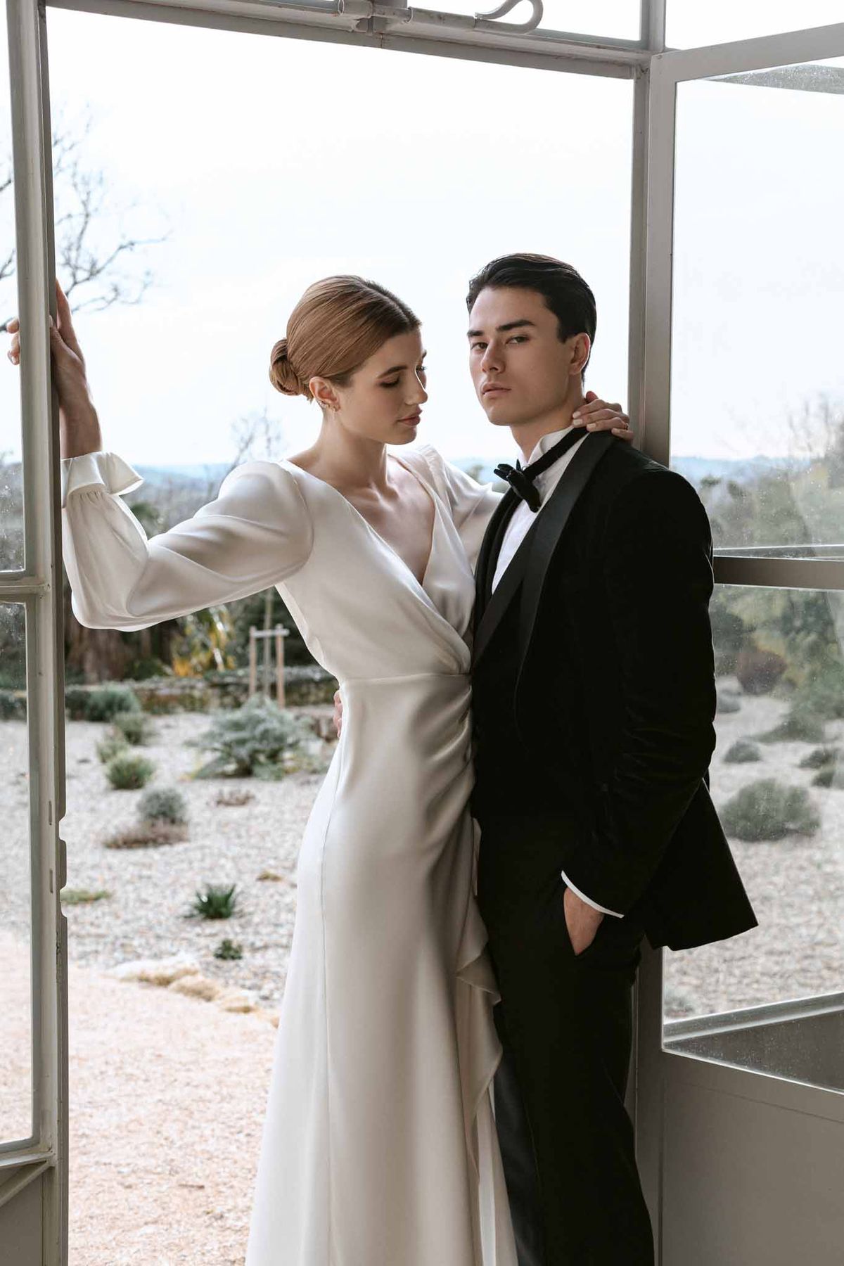 Bride and groom posing inside glass-walled structure during winter wedding