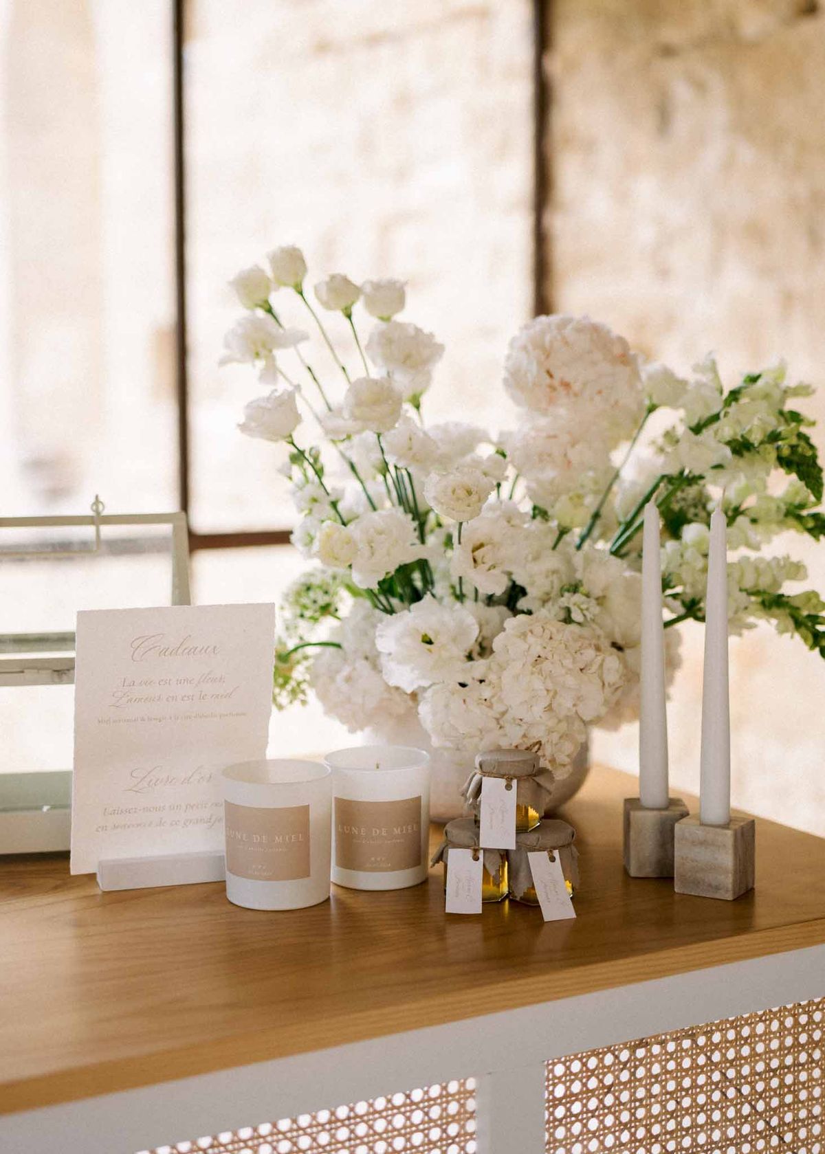 Gift table with white hydrangea arrangement Lune de Miel candle favors honey jars and Cadeaux signage at stone venue