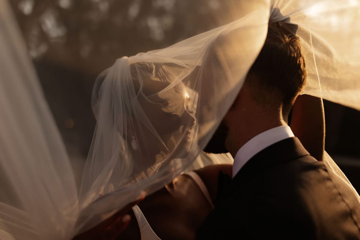 Bride and groom portrait with flowing ivory veil at outdoor garden wedding during golden hour