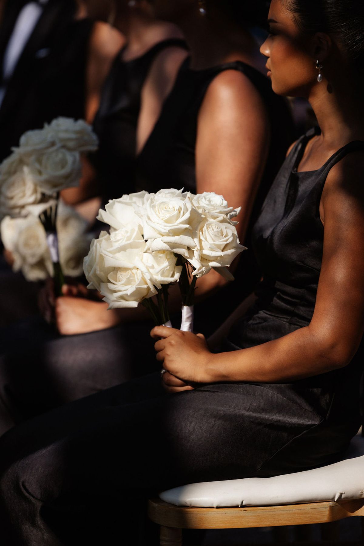 Bridesmaid in black dress holding ivory rose bouquet at indoor wedding ceremony