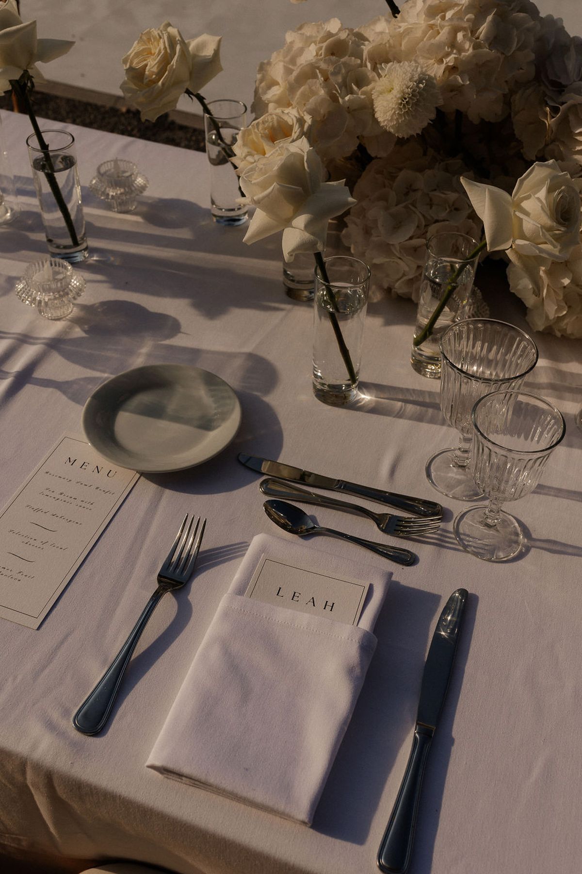 Elegant white and black table setting with cream roses and clear glassware for wedding reception