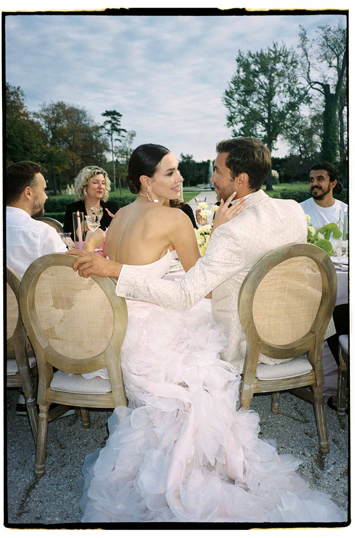 Bride and groom dining with guests at outdoor reception table overlooking lake