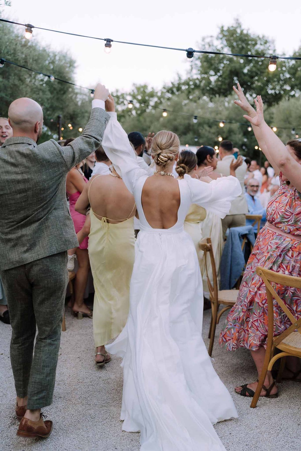 Bride and groom first dance surrounded by guests at outdoor garden reception with string lights