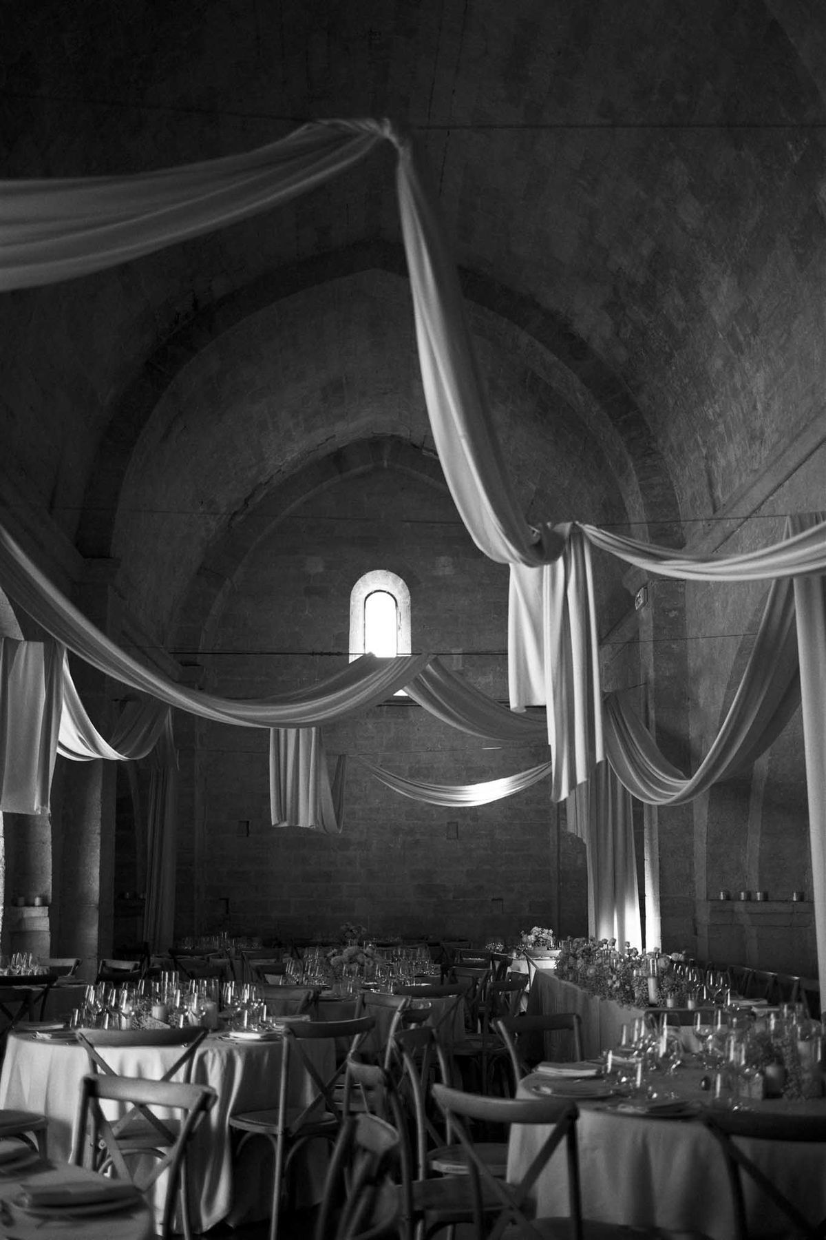 Barrel-vaulted stone chapel with white ceiling drapes and round reception tables in B&W