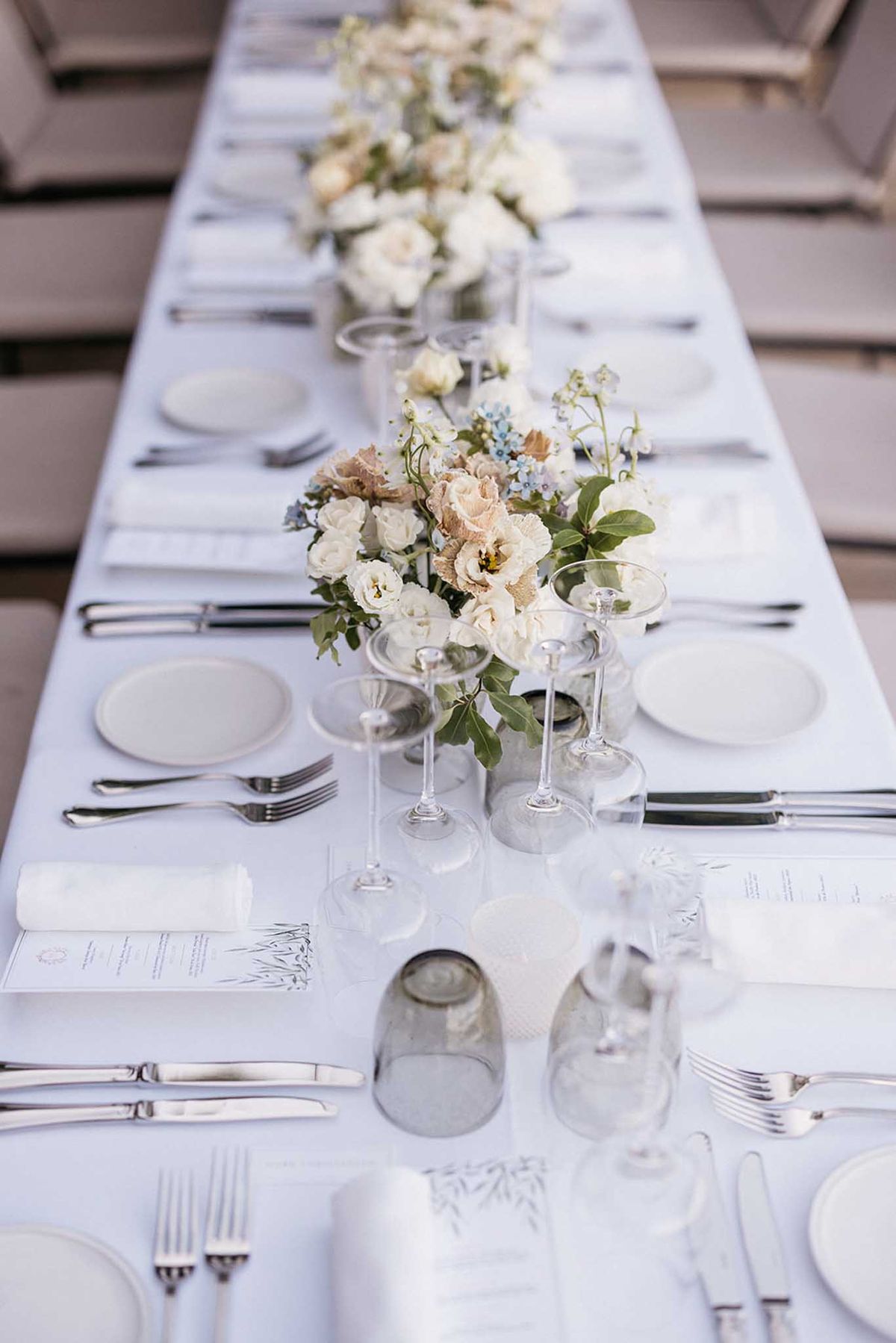 Long banquet table with floral centerpieces and formal place settings at indoor wedding reception