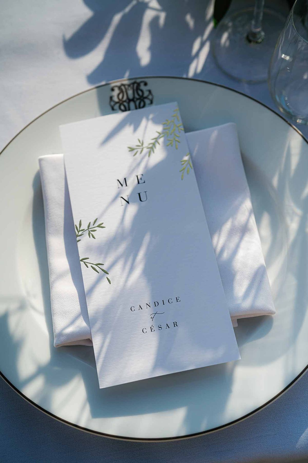 Wedding menu card with olive branch design on place setting at outdoor reception table