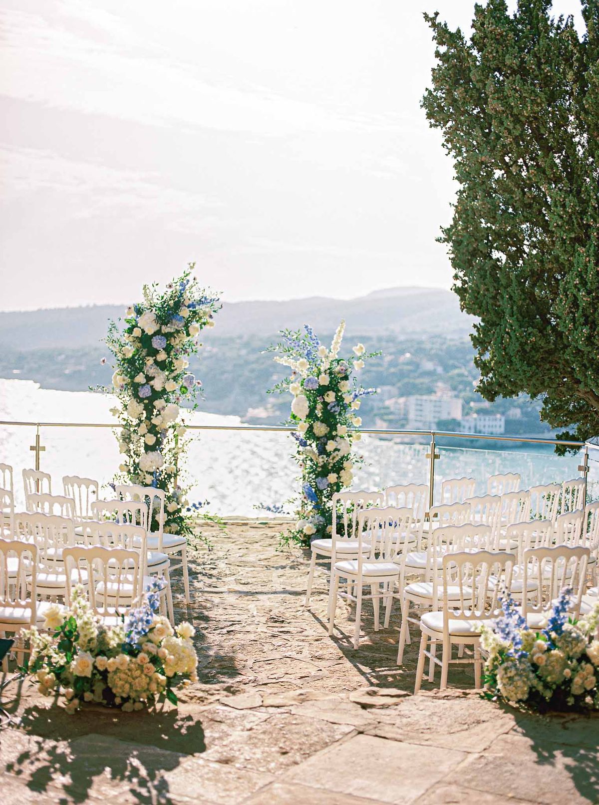 Outdoor wedding ceremony setup with floral pillars overlooking lake at terrace venue