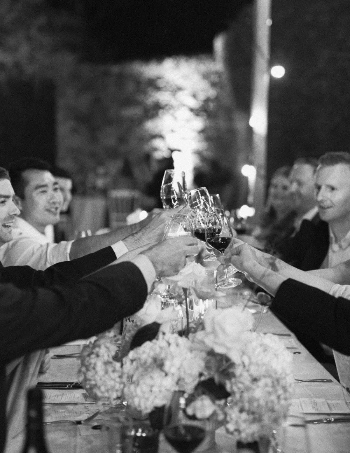 Wedding guests raising wine glasses in toast at outdoor reception dinner table