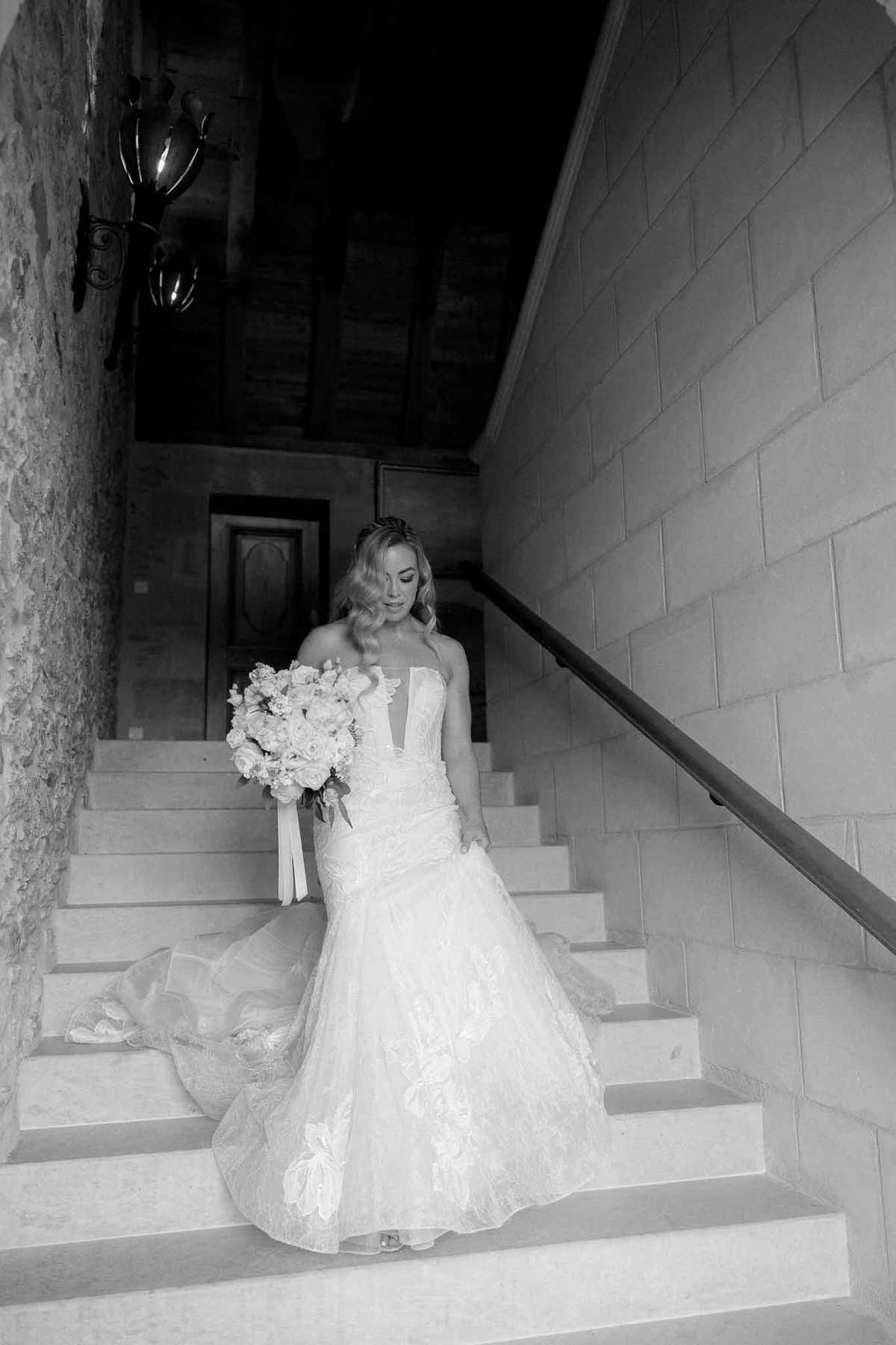 Bride in mermaid gown descending stone staircase in modern architectural venue