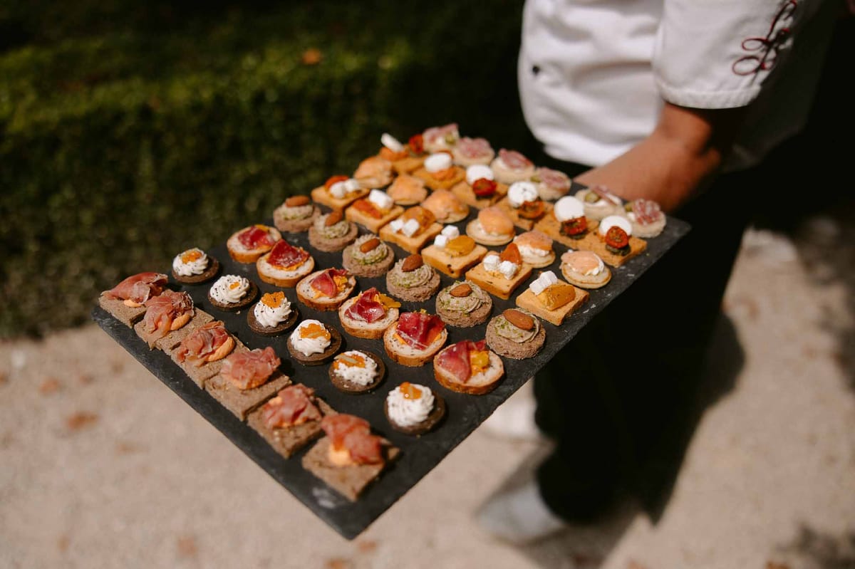 Server holding slate board of assorted canapes including rye bread rounds and smoked salmon bites
