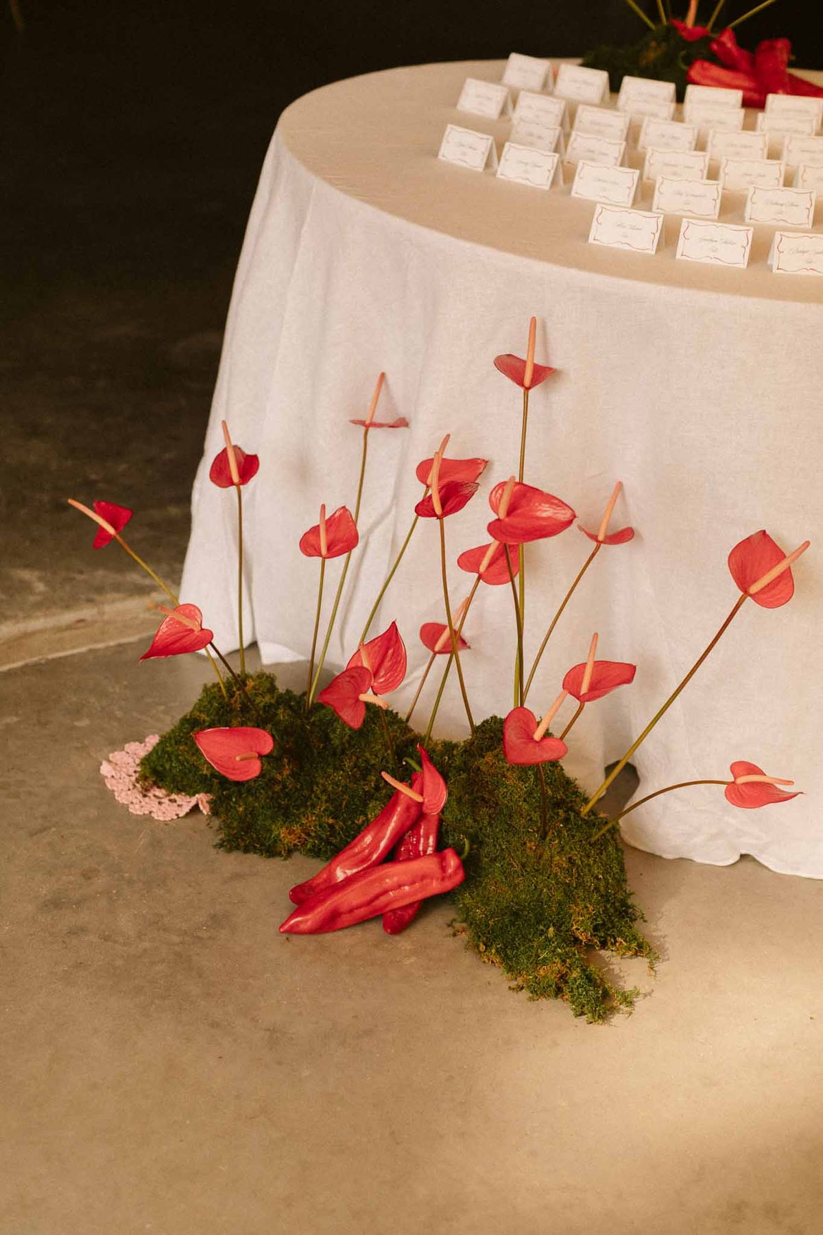Seating card display with red anthurium floral centerpiece at indoor wedding reception