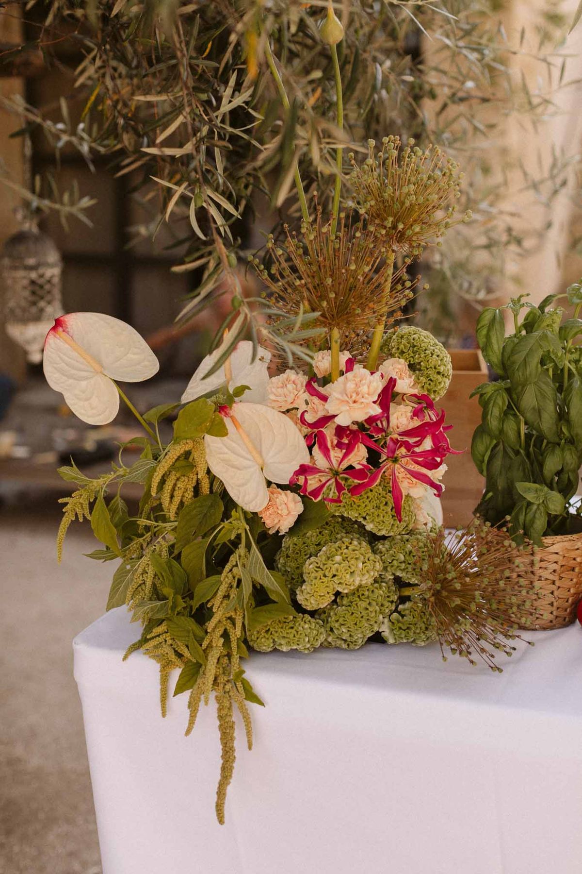 Wedding floral arrangement with anthurium and burgundy astilbe on white-draped table at reception venue