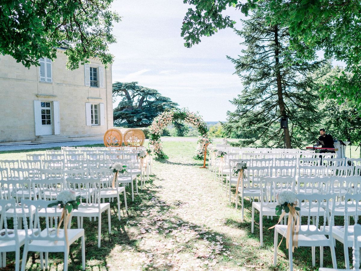 Pre-ceremony setup with circular blush rose arch, rattan peacock chairs, and white chairs facing countryside