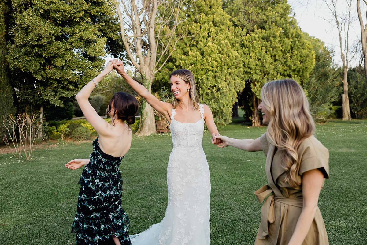 Bride dancing with guests during outdoor reception on manicured lawn with mature trees
