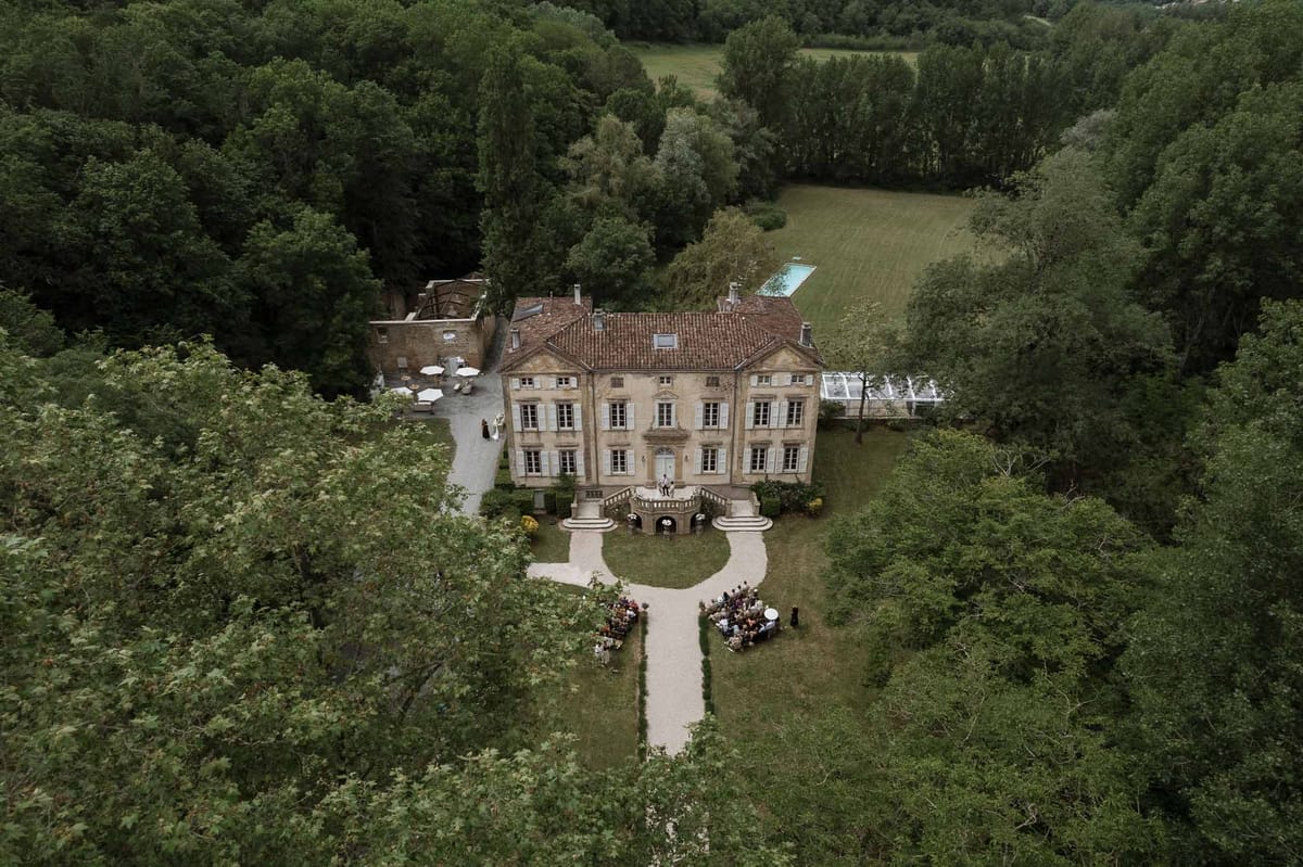 Aerial view of outdoor wedding ceremony at stone château with guests seated on manicured lawn