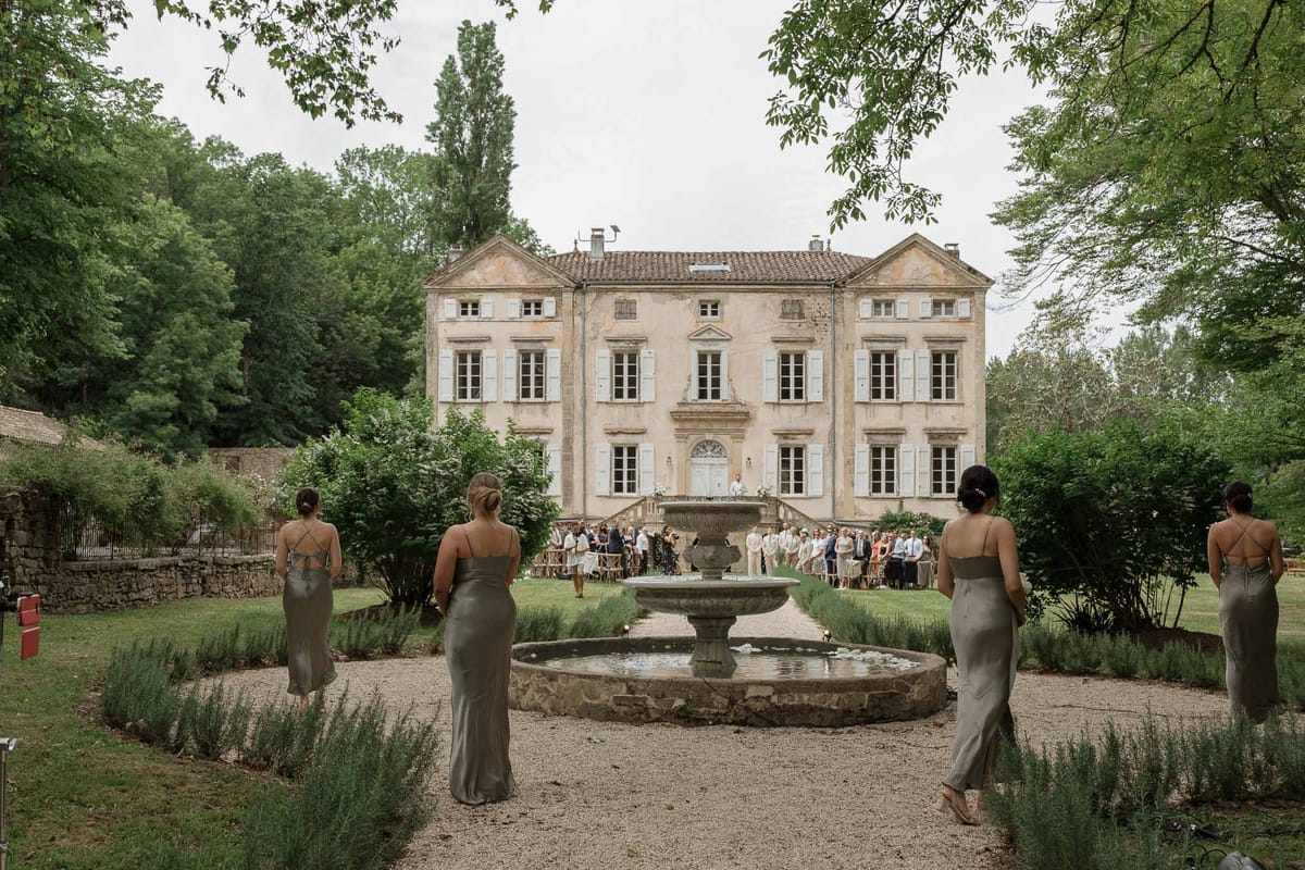 Bridal party in sage green dresses by stone fountain at French château gardens