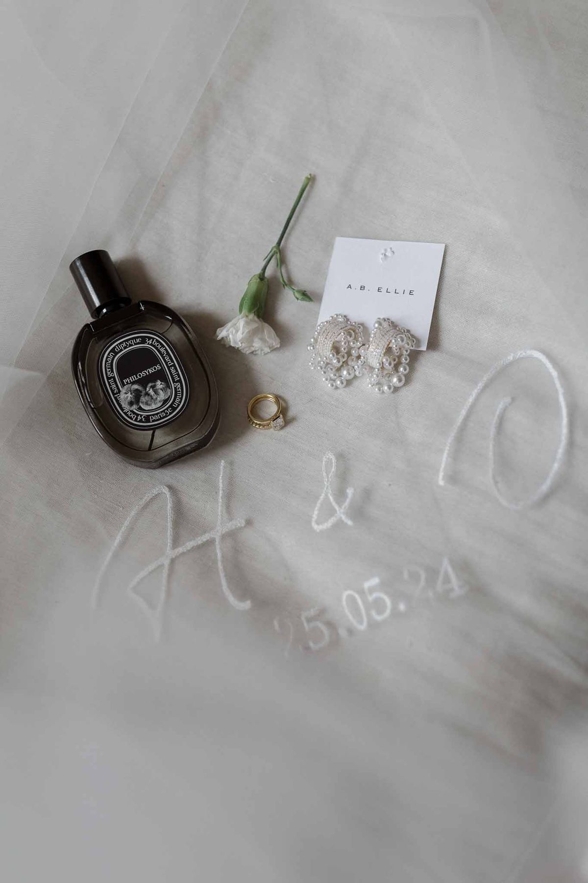 Wedding accessories flat lay with perfume, jewelry and rings on ivory tulle fabric