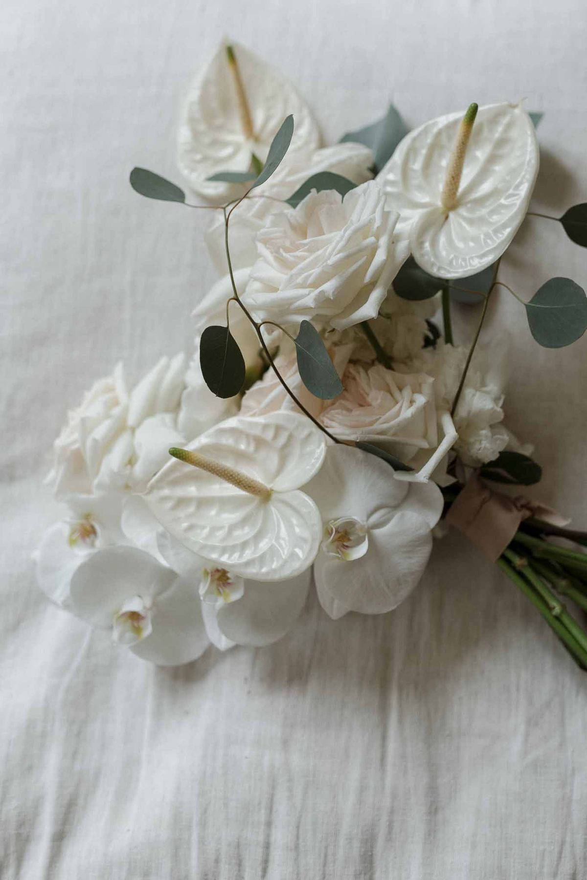 White bridal bouquet with garden roses and orchids arranged on white linen fabric