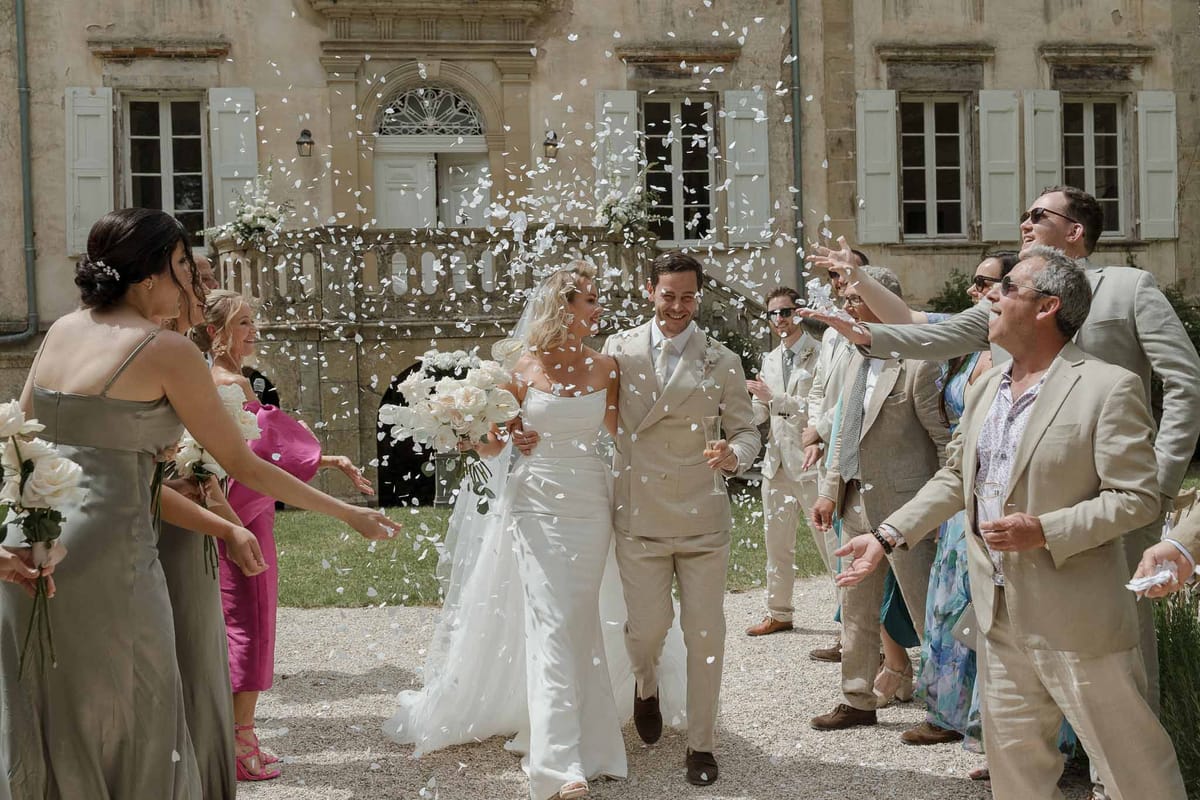 Couple exits ceremony through petal toss at classical stone mansion courtyard