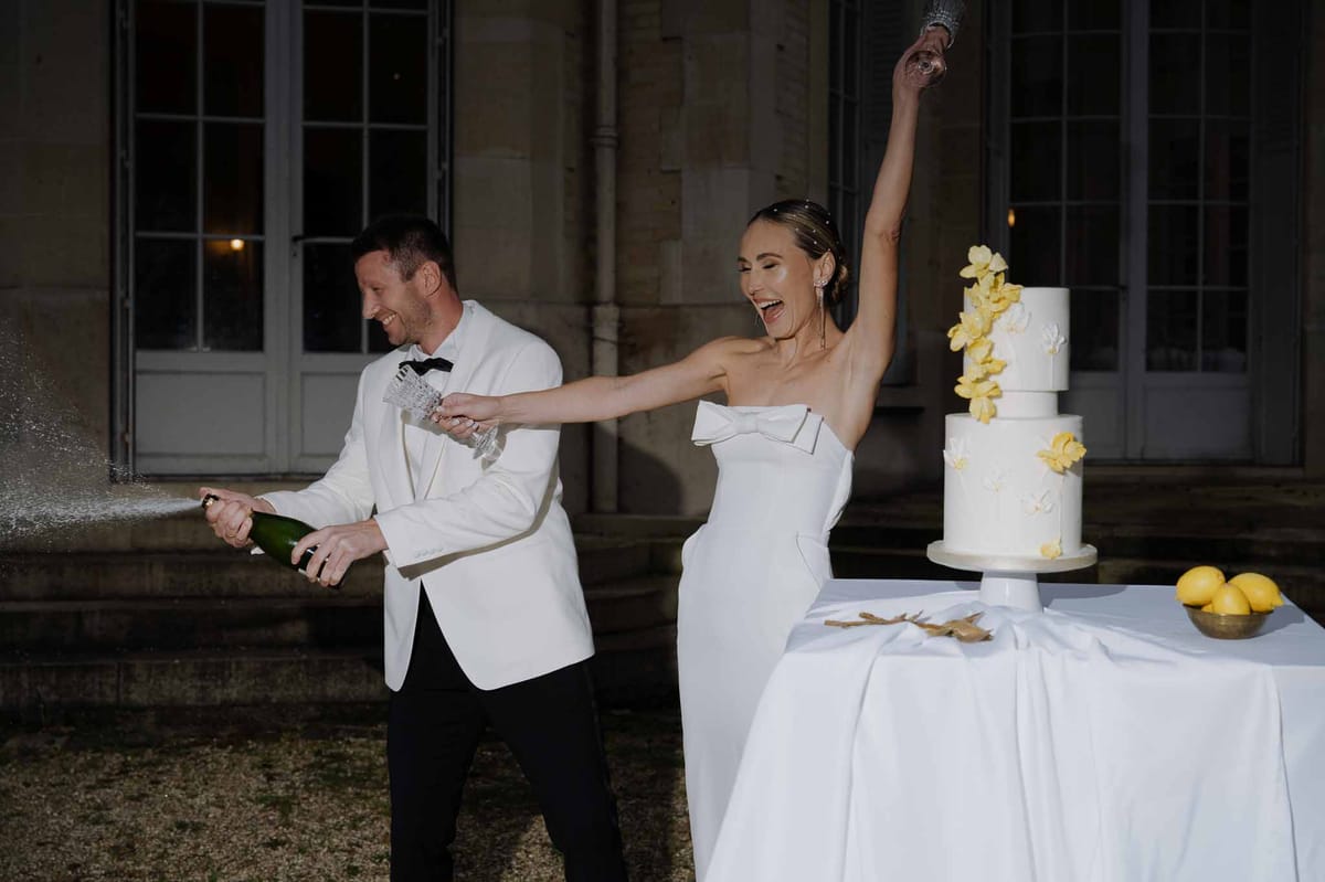 Bride and groom spraying champagne during outdoor reception at industrial courtyard venue