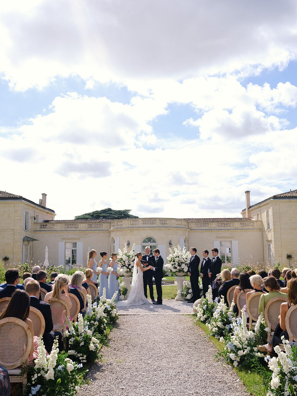 70 guests at chateau ceremony with white delphinium aisle flowers and bridesmaids in blue-grey gowns