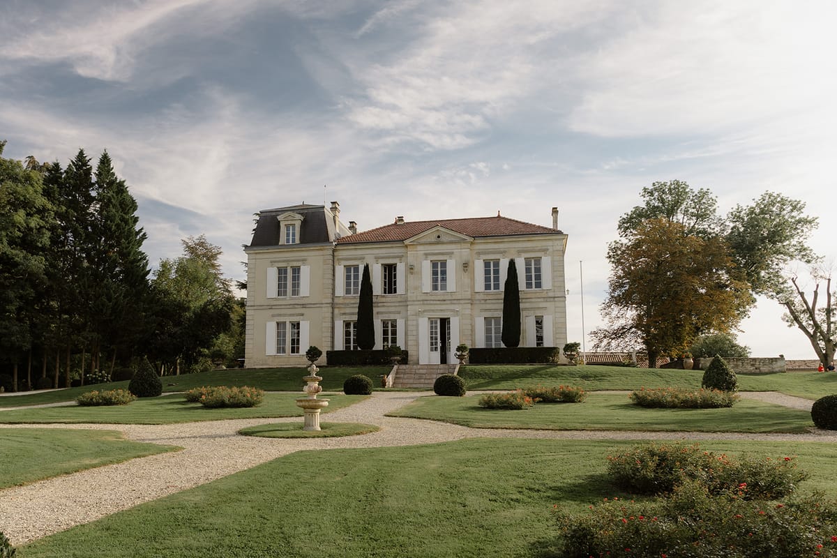 French chateau with cream limestone facade, formal garden with rose beds, box hedging, stone fountain, and cypress trees