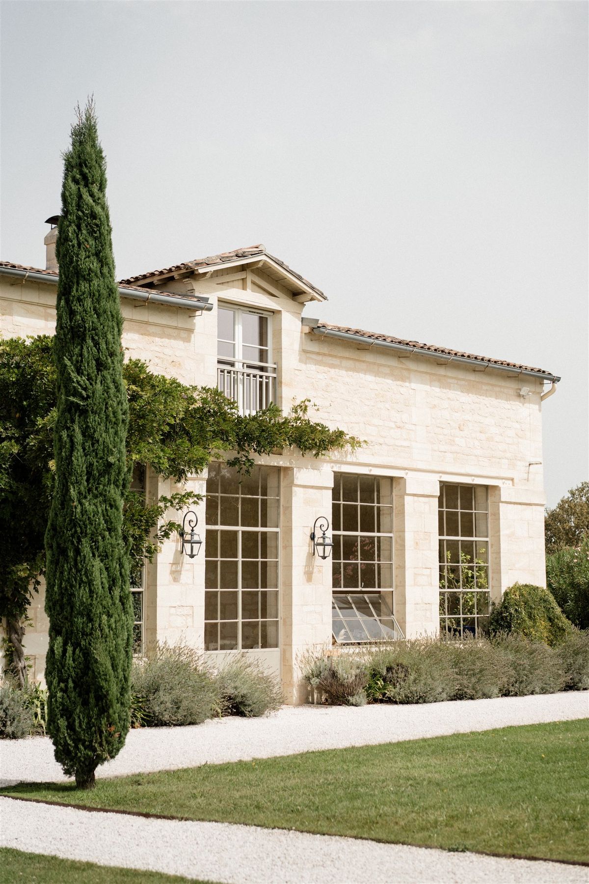 Cream limestone estate with steel-framed windows, black lanterns, climbing greenery, and central dormer