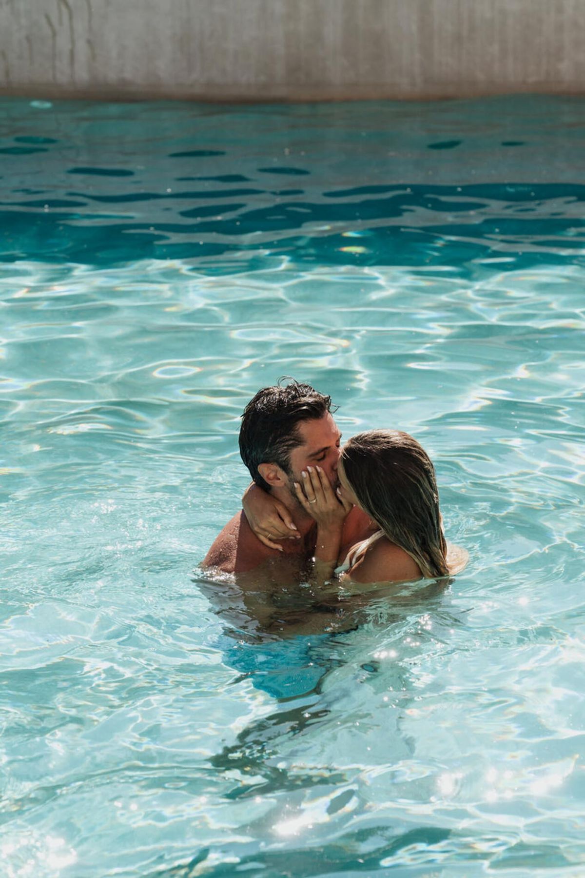 Couple kissing in turquoise pool with wet hair during relaxed post-wedding portrait session