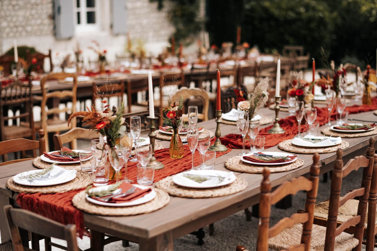 Autumn reception table with terracotta runner red gerberas amber vases brass candlesticks and rush-seat chairs