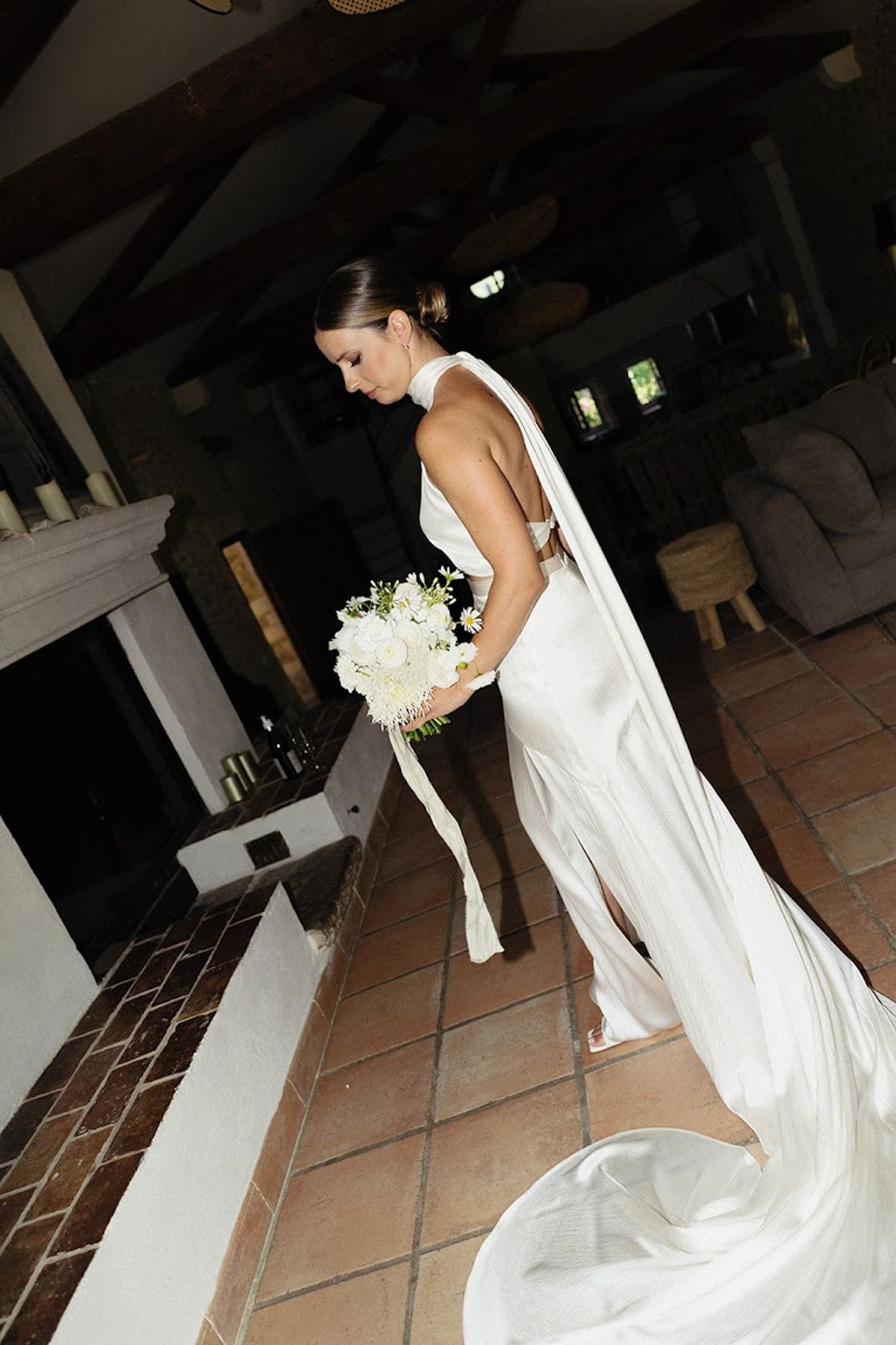 Bride in ivory halter gown with protea and ranunculus bouquet in rustic farmhouse with terracotta tiles