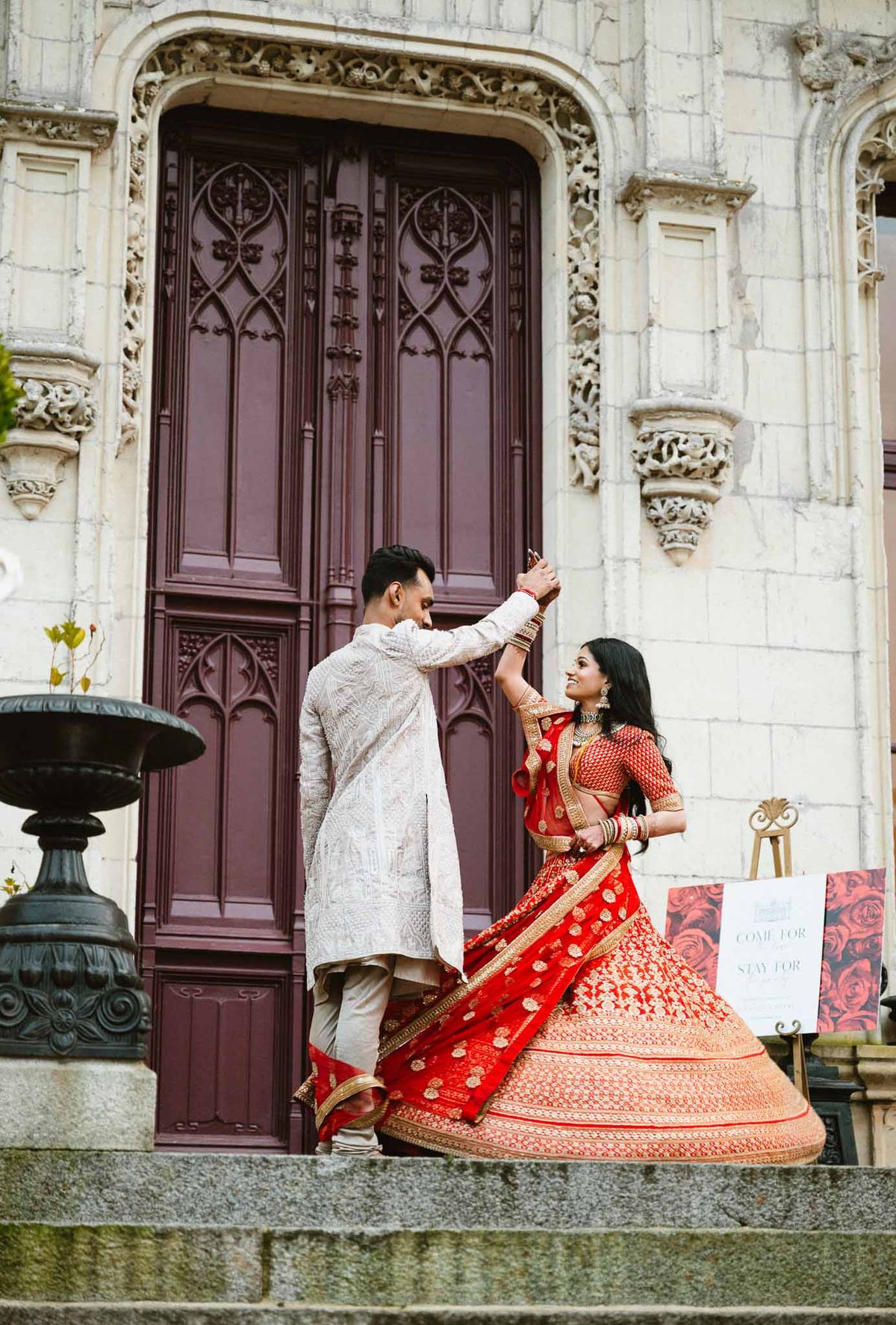 Indian wedding couple portrait in traditional attire at neoclassical stone building with burgundy doors