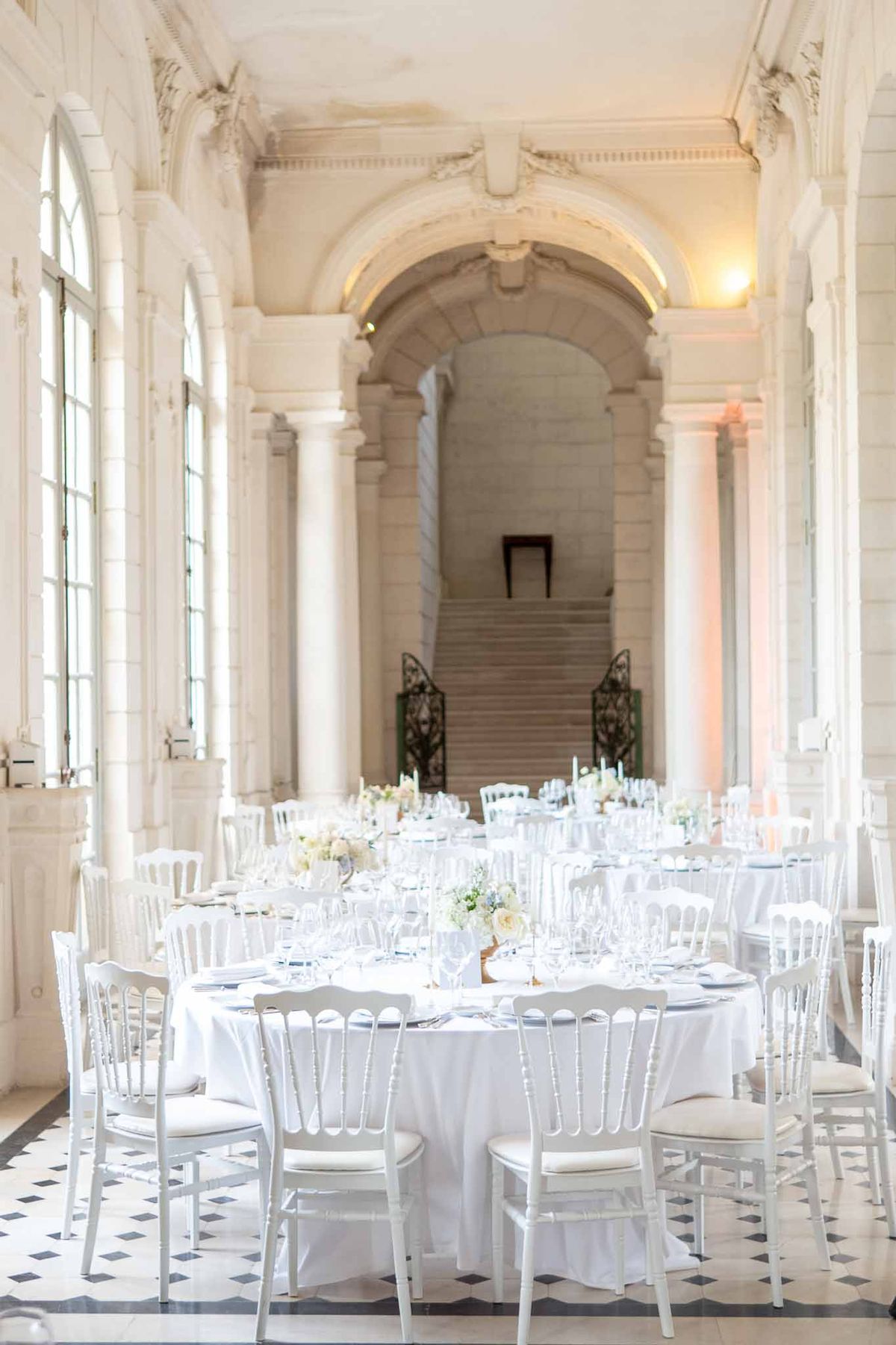 Wedding reception setup with white linens and floral centerpieces in classical columned hall