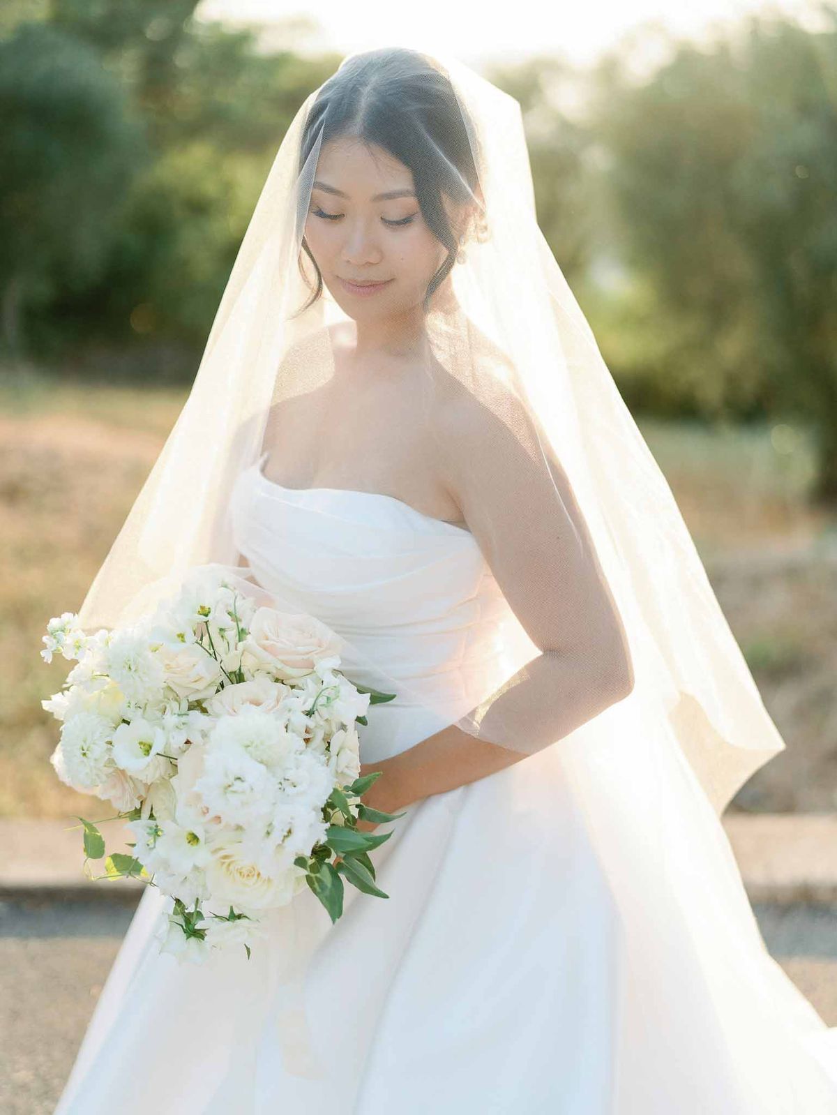 Bride in ivory strapless gown with white bouquet poses in garden during golden hour