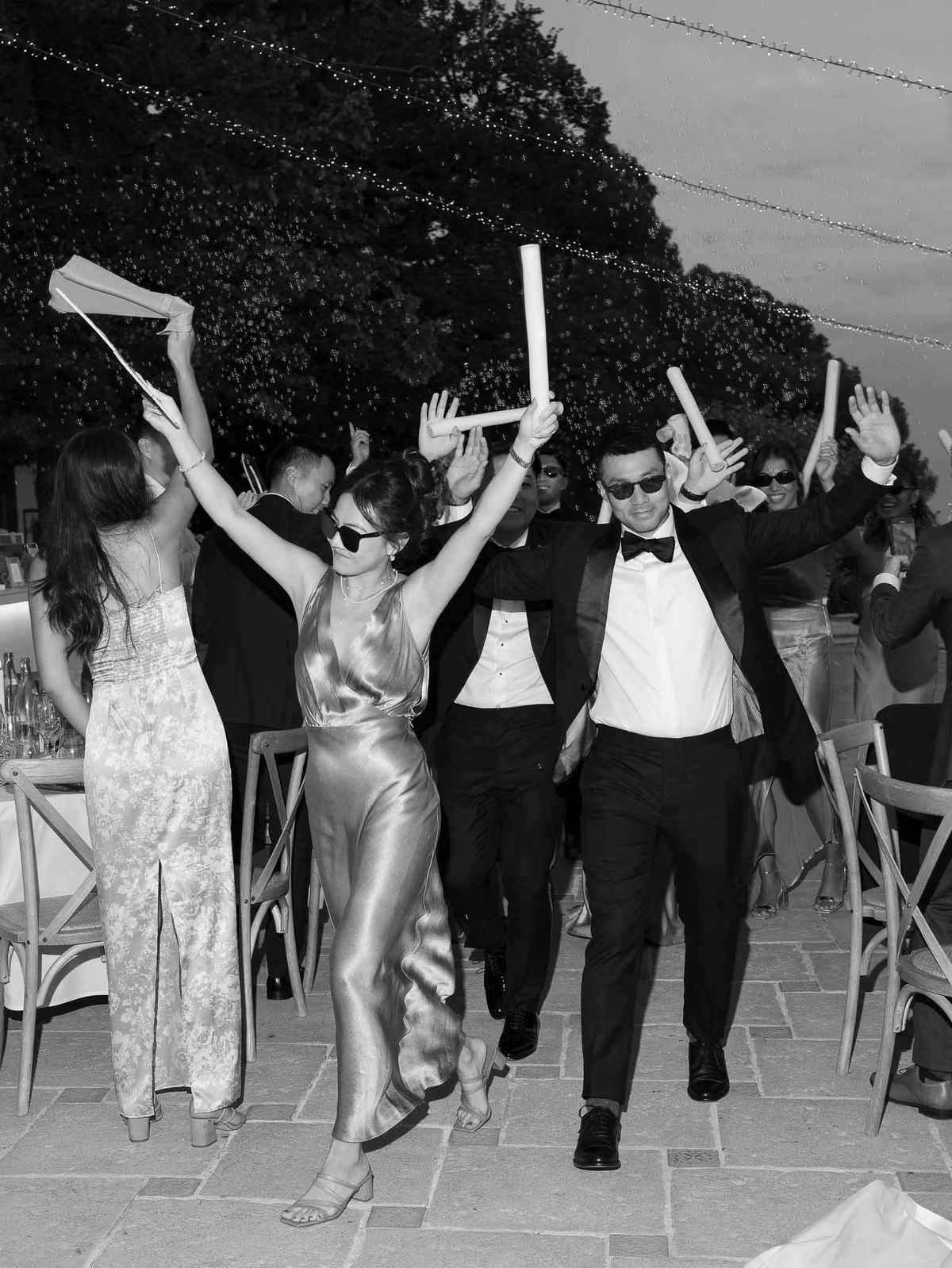 Bride and groom leading sparkler exit celebration with guests on outdoor terrace at wedding reception